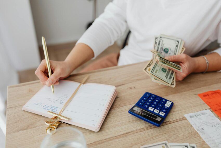 person writing on a notebook while holding money