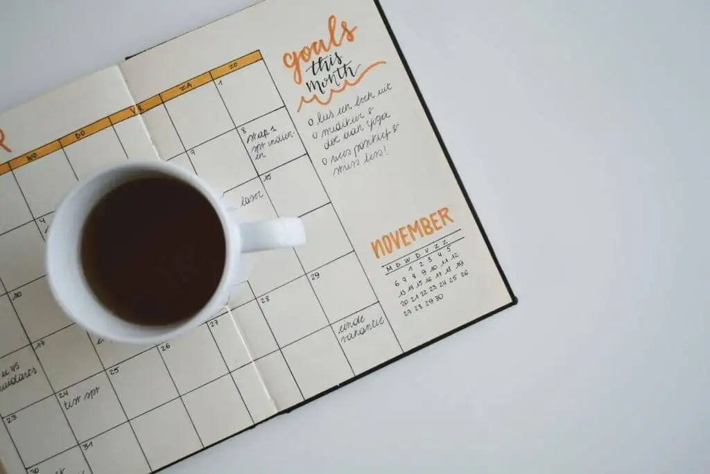 A cup of coffee laying on a calendar used for setting short-term financial goals and long-Term Financial Goals