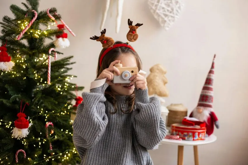 Creative Holiday Gifts Kids Will Love That Won't Break The Bank: a young girl with a camera toy against christmas tree