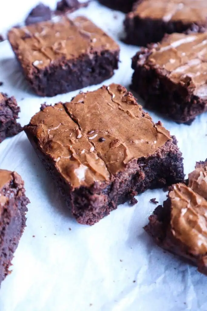 A batch of rich, fudgy chocolate brownies with a crackly top, cut into squares and displayed on parchment paper. This classic Valentine's Day dessert is perfect for chocolate sweets enthusiasts who crave a decadent and indulgent treat.