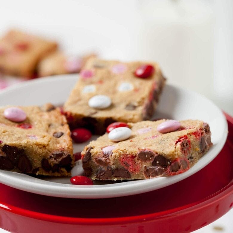 Chewy Blondies studded with colorful Valentine’s candies and chocolate chips, served on a white plate, a fun and festive option for Valentine's Dessert Ideas.