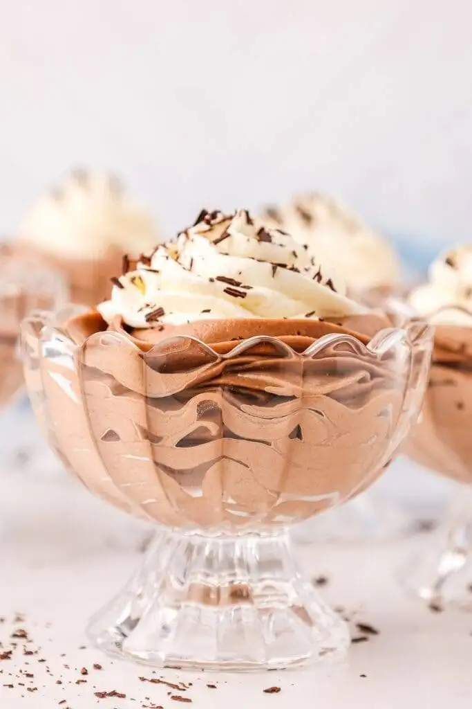 A close-up of an elegant Valentine's Day dessert featuring rich, creamy chocolate mousse in a decorative glass dish, topped with fluffy whipped cream and sprinkled with delicate chocolate shavings, making it a perfect treat for chocolate sweets lovers.