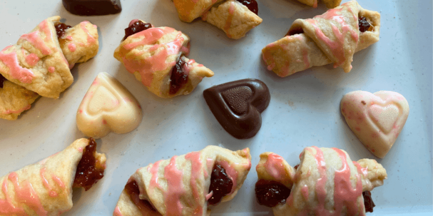 Strawberry Rugelach drizzled with pink icing alongside a heart-shaped chocolate, a festive and delicious choice for Valentine's Dessert Ideas.