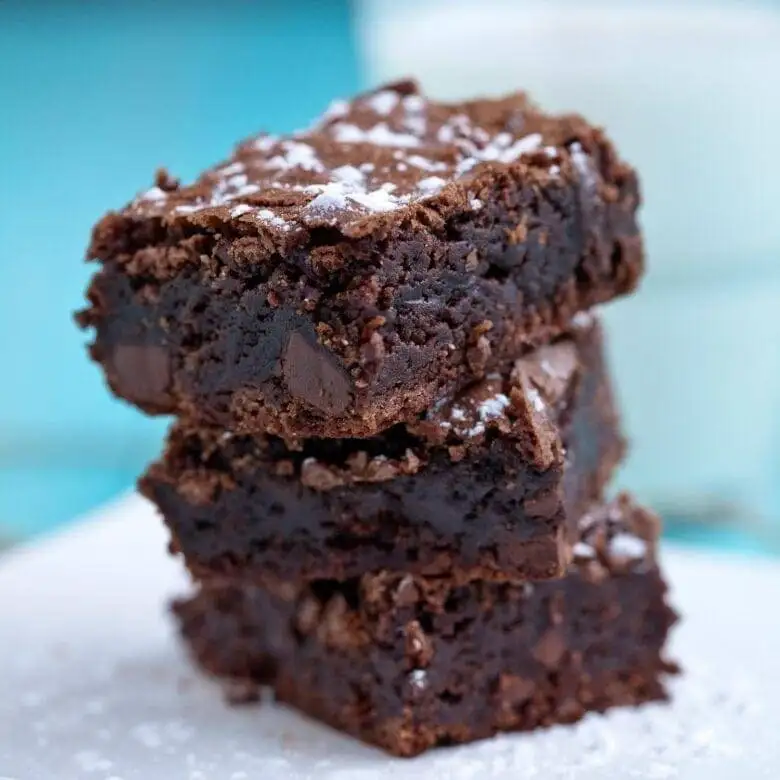 A stack of rich, gooey chocolate brownies loaded with chocolate chunks, dusted lightly with powdered sugar. This indulgent Valentine's Day dessert is a heavenly choice for chocolate sweets enthusiasts looking to share a decadent treat.