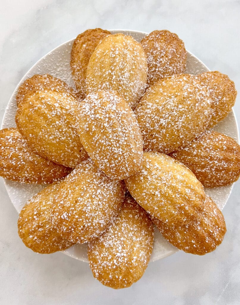 Vegan Madeleines arranged on a white plate, dusted with powdered sugar, a sophisticated and elegant option for Valentine's Dessert Ideas.