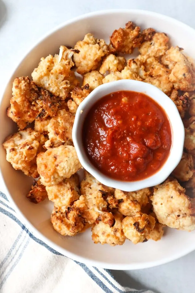 A bowl of crispy cauliflower bites served with a side of marinara sauce, perfect for dipping. A healthy and flavorful Super Bowl food idea for game day snacking.