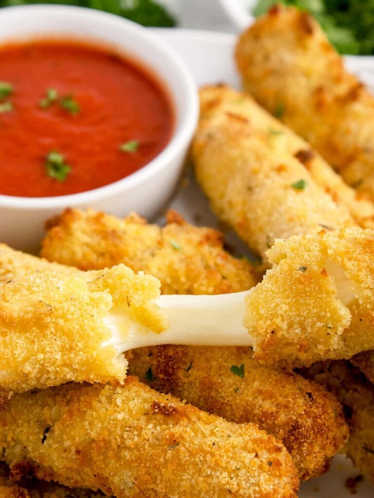 Golden, crispy mozzarella sticks with a gooey cheese pull, served alongside a bowl of marinara sauce for dipping. These classic and indulgent treats are a popular choice for a Superbowl appetizer.