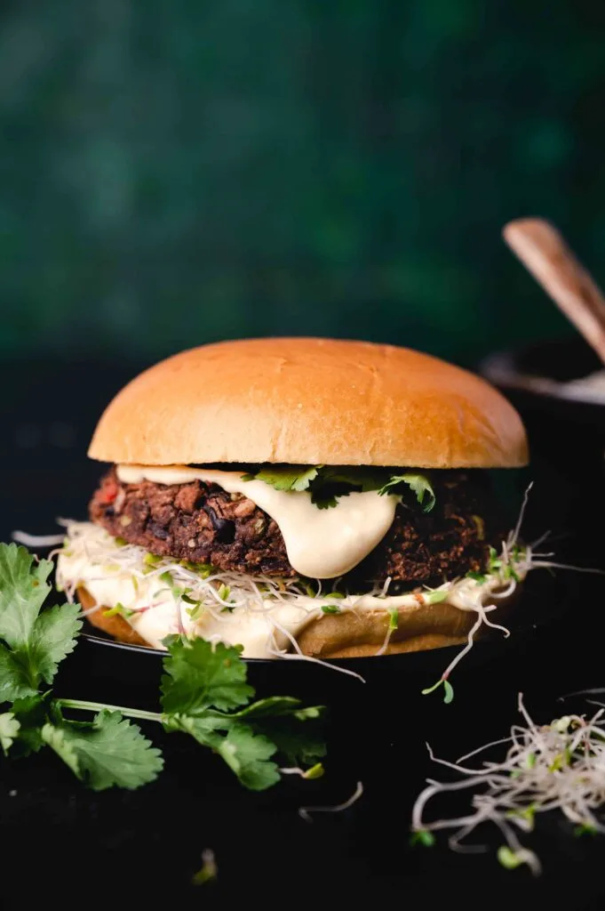 A gourmet black bean burger topped with sprouts, fresh cilantro, and creamy sauce, served on a soft bun. A flavorful and healthy Super Bowl food idea for plant-based game day options.