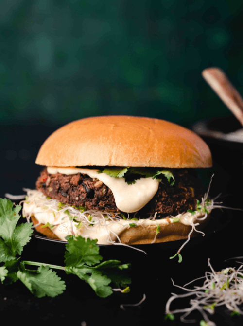 Black bean veggie burger topped with creamy sauce, sprouts, and cilantro on a toasted bun—hearty and wholesome option for Super Bowl food ideas.