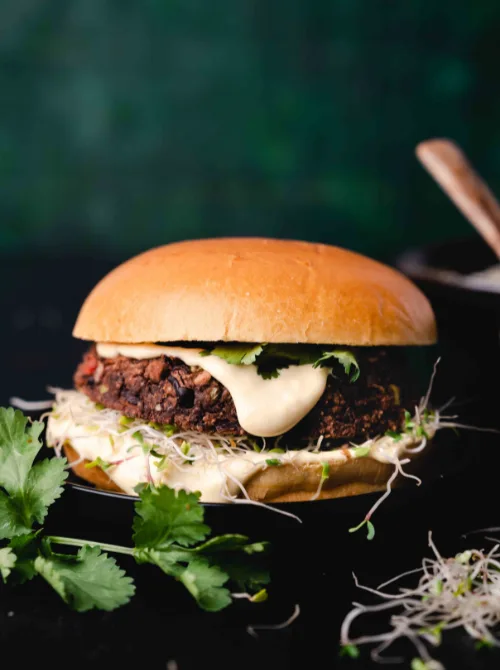 Black bean veggie burger topped with creamy sauce, sprouts, and cilantro on a toasted bun—hearty and wholesome option for Super Bowl food ideas.