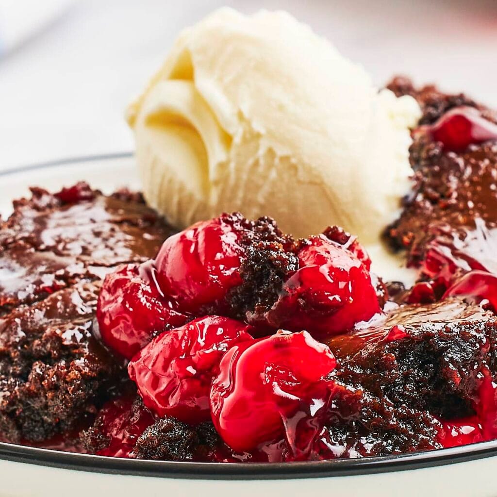 Close-up of a rich chocolate cherry cake served with a scoop of vanilla ice cream, showcasing a decadent option for Valentine's Cake Ideas with its vibrant red cherries and indulgent chocolate base.