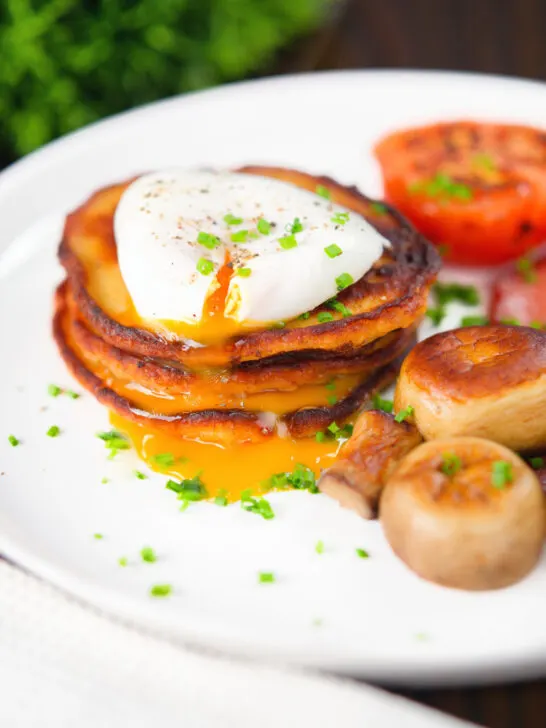 Plate of golden Irish potato pancakes topped with a perfectly poached egg and garnished with fresh chives, served alongside sautéed mushrooms and roasted tomatoes—ideal for St. Patrick's Day food ideas and classic Irish recipes.