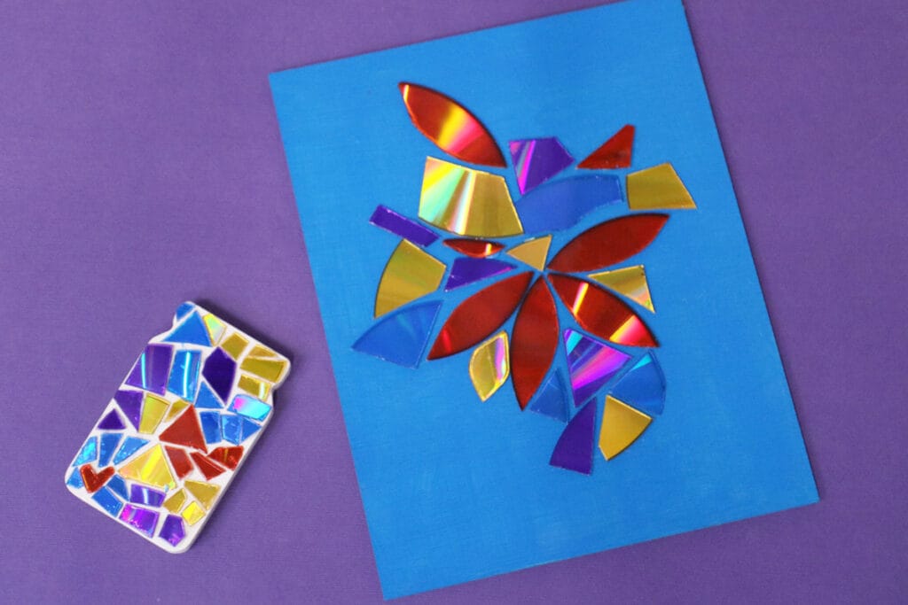 A vibrant DIY mosaic craft featuring colorful, reflective shapes arranged on a blue background, alongside a decorated phone case with a similar mosaic design. A playful and creative project for DIY Valentine's Crafts, perfect for personalized and artistic gifts.