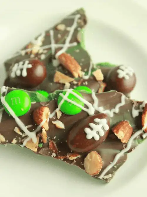 Chocolate football bark topped with green and brown M&M candies, almonds, and white icing football laces—fun and festive treat for game day parties.