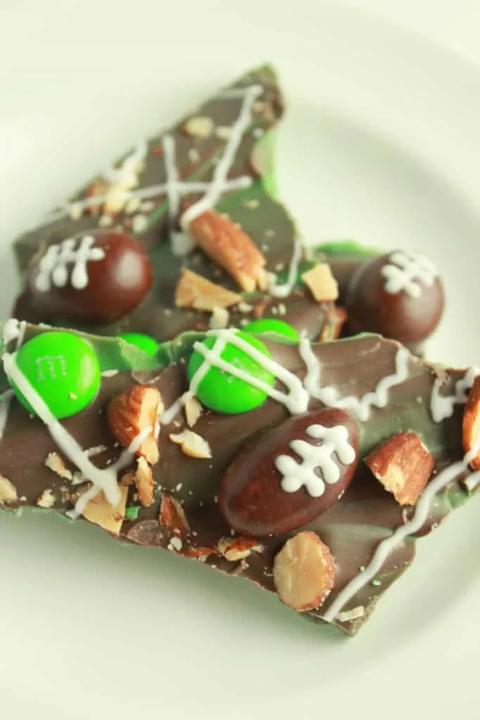 Football-themed chocolate bark topped with green and brown candies, decorated like footballs, and sprinkled with chopped almonds. A fun and sweet Super Bowl food idea for game day treats.