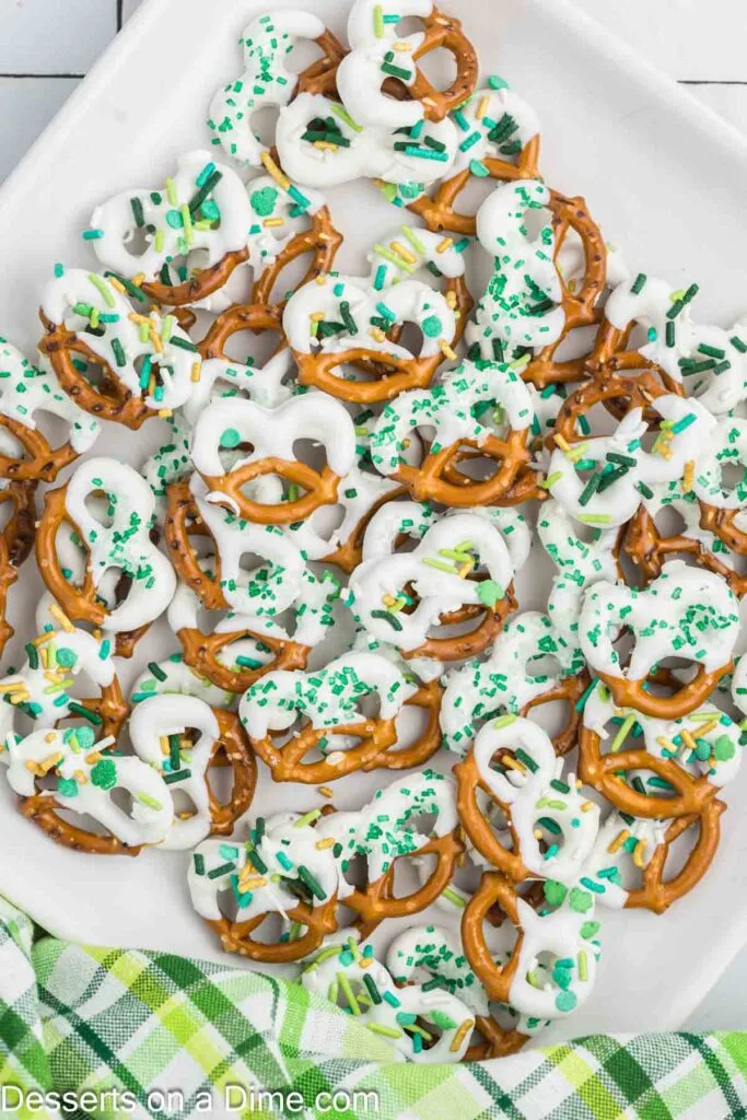 A plate of festive pretzels dipped in white chocolate and topped with green and yellow sprinkles, perfect for St Patrick's Day desserts or Irish-themed snacks.