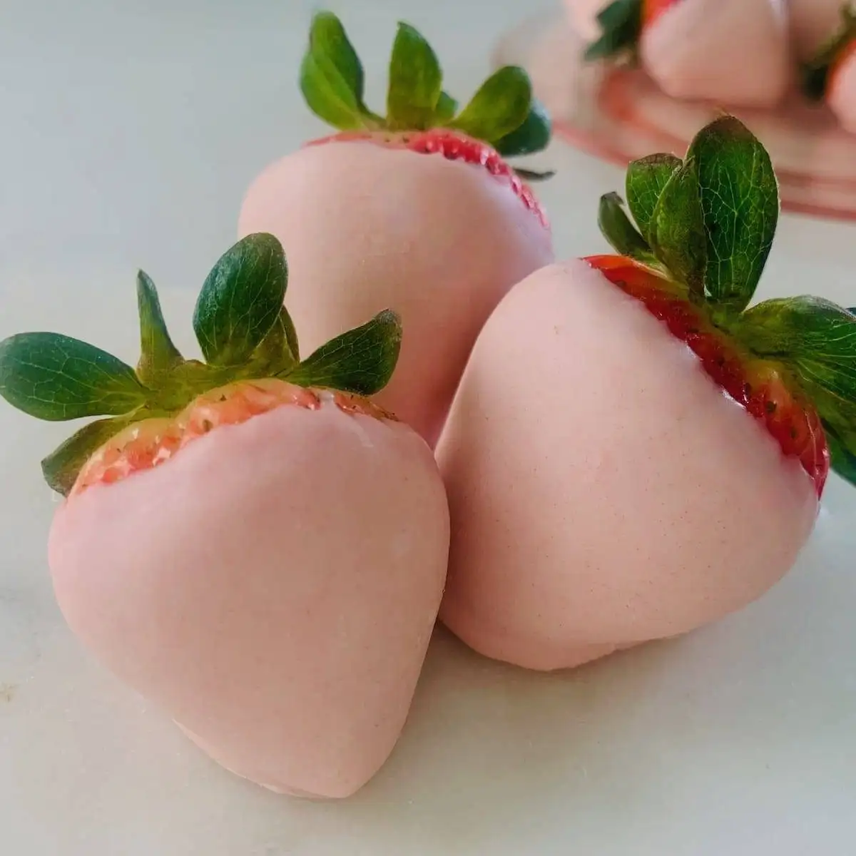 Fresh strawberries dipped in pale pink chocolate with green stems intact, creating an elegant and sweet treat perfect for romantic desserts for two or special occasions.