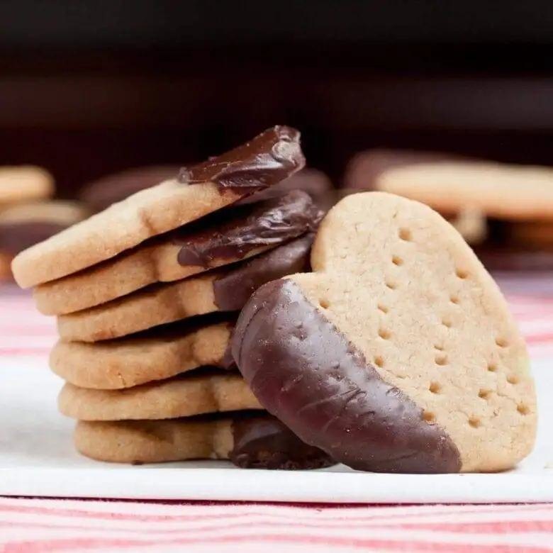 A stack of buttery shortbread heart cookies, each partially dipped in rich, glossy chocolate, offering a simple yet indulgent treat for Valentine's Day.