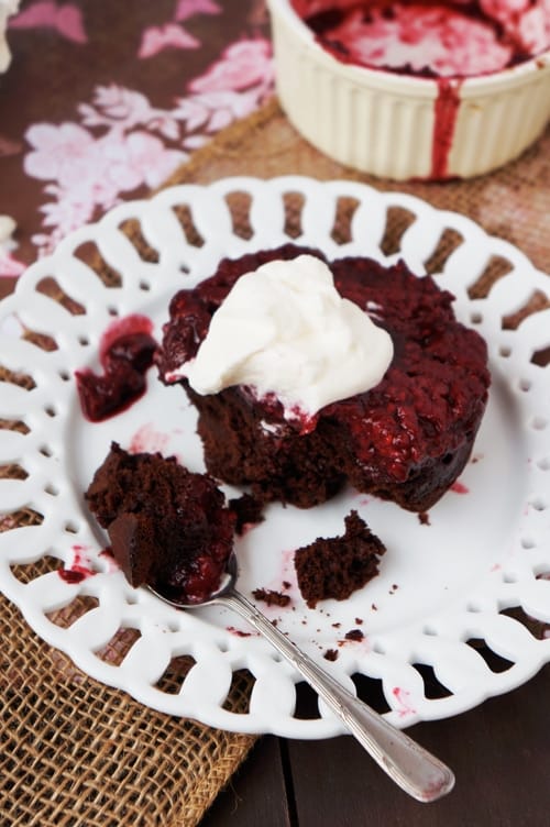 Rustic presentation of a rich chocolate cake topped with raspberry sauce and whipped cream on a decorative white plate, making it an elegant and romantic option for Valentine's Cake Ideas.