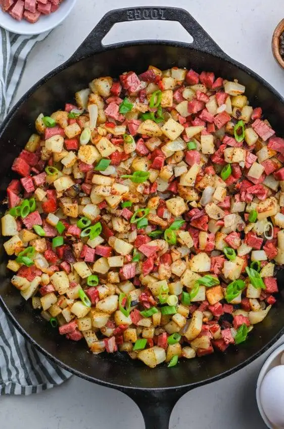 Skillet filled with crispy corned beef hash made with diced potatoes, onions, and corned beef, garnished with fresh green onions—perfect for St. Patrick's Day food ideas and hearty Irish-inspired recipes.