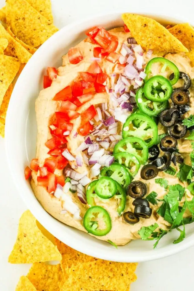 Vibrant seven-layer dip topped with fresh tomatoes, onions, jalapeños, olives, and cilantro, served with tortilla chips—a colorful favorite among the best party dips.