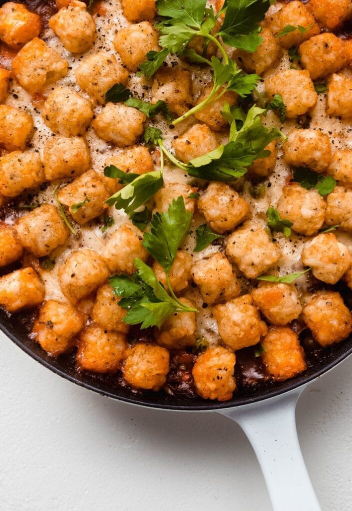 Skillet filled with a twist on shepherd's pie, topped with crispy tater tots and garnished with fresh parsley—an innovative dish perfect for St. Patrick's Day food ideas and modern Irish-inspired recipes.S