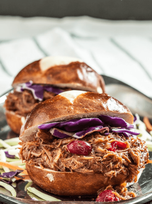 Close-up of pulled pork sliders on soft pretzel buns, topped with tangy red cabbage and cranberries—a delicious and creative way to repurpose leftovers recipes.