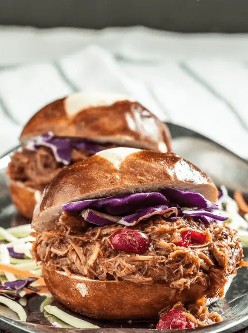 Close-up of pulled pork sliders on soft pretzel buns, topped with tangy red cabbage and cranberries—a delicious and creative way to repurpose leftovers recipes.