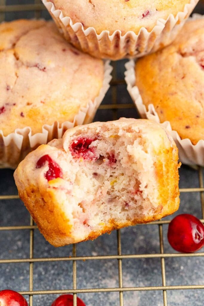 Close-up of fluffy cranberry muffins with a tender crumb, one with a bite taken out, showcasing juicy cranberries—an easy and sweet option for creative leftovers recipes.