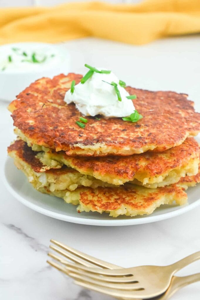 Stack of crispy Irish potato pancakes topped with sour cream and fresh chives, served alongside a creamy dipping sauce—perfect for St. Patrick's Day food ideas and traditional Irish recipes.