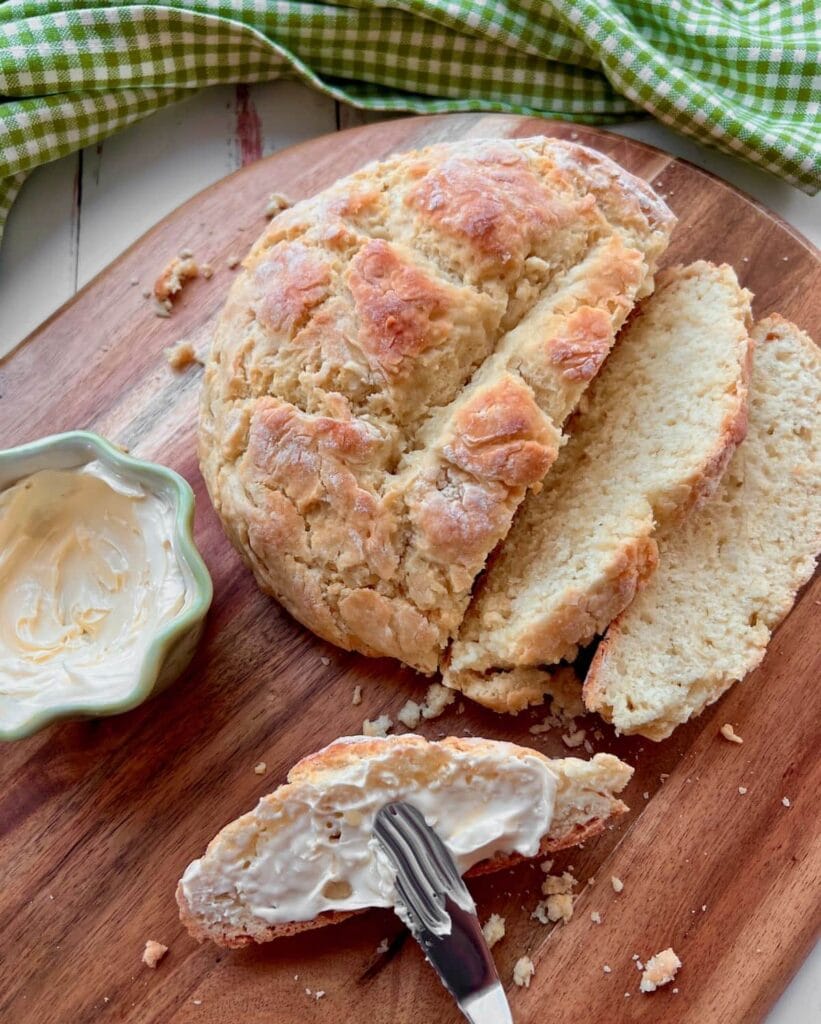 Rustic Irish soda bread sliced on a wooden cutting board, served with creamy butter spread—perfect for St. Patrick's Day food ideas and traditional Irish recipes.