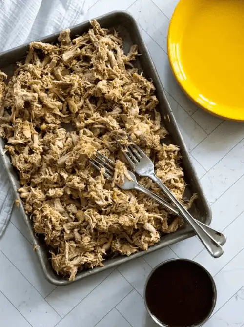 Shredded Dutch oven pulled chicken served on a baking tray—versatile and budget-friendly Super Bowl food idea perfect for sliders or wraps.