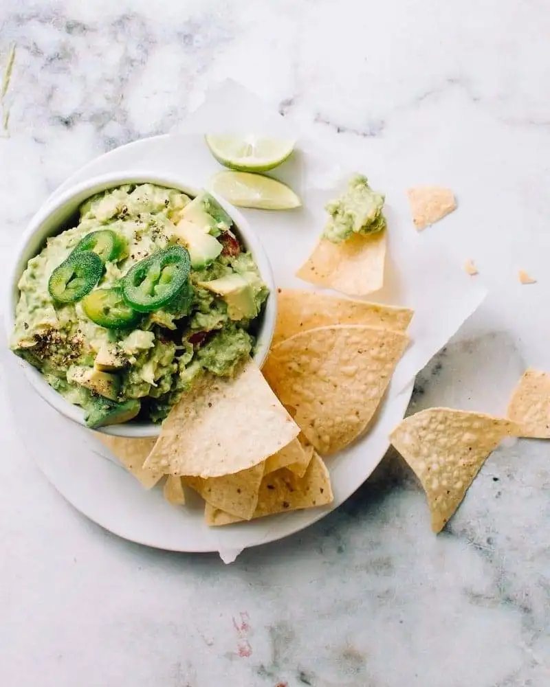 Fresh guacamole topped with sliced jalapeños and served with crispy tortilla chips and lime wedges, a vibrant addition to the best party dips spread.