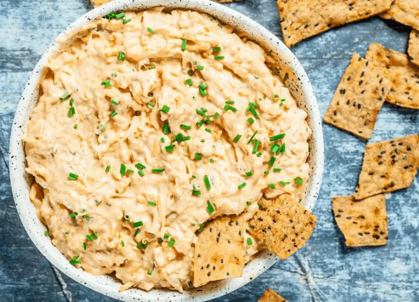 Creamy buffalo chicken dip topped with chopped chives, served with seeded crackers—a crowd-pleaser among the best party dips.