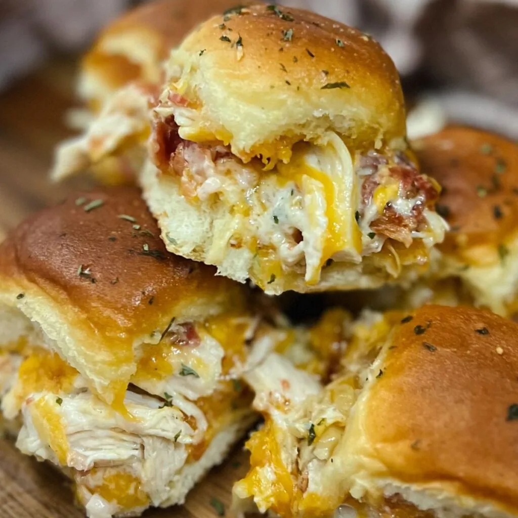 Cheesy pulled chicken sliders topped with crispy bacon, served on buttery rolls and garnished with herbs. A delicious and easy Super Bowl food idea for a crowd-pleasing game day treat.