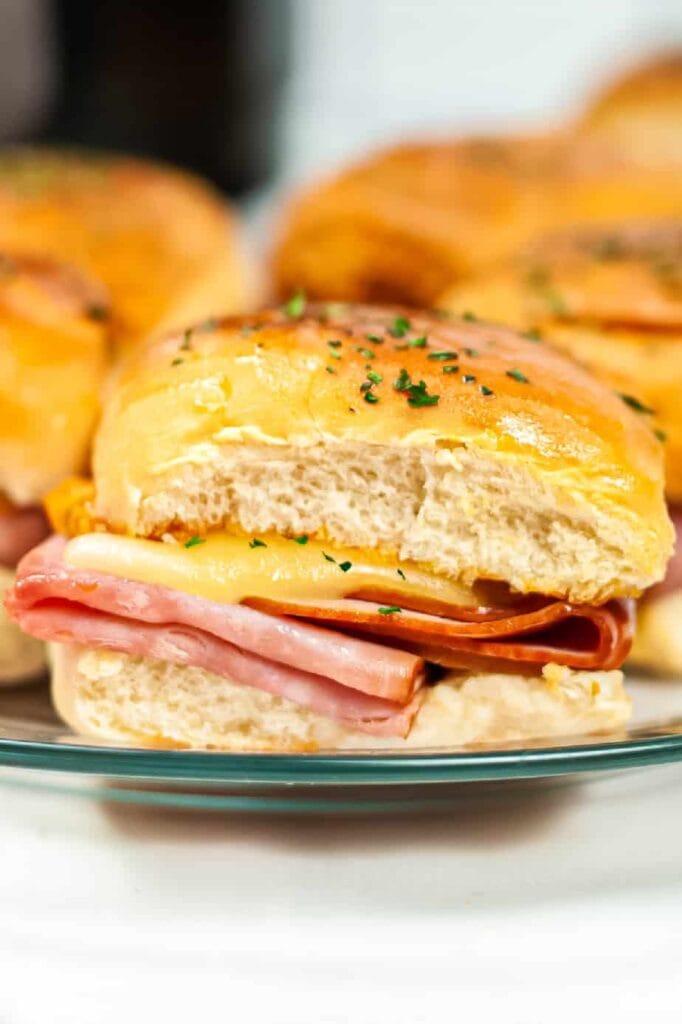 Warm ham and cheese sliders on soft buns, topped with a buttery garlic glaze and sprinkled with fresh parsley, perfect for quick and easy appetizers or meals.