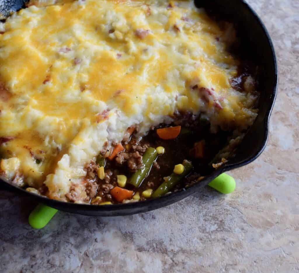 Skillet of cheesy shepherd's pie with a golden mashed potato topping, revealing a savory filling of ground meat and mixed vegetables—an ultimate comfort food made from leftovers recipes.