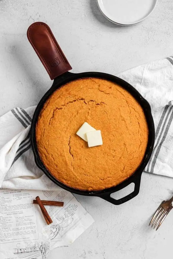 Golden-brown cornbread baked in a cast iron skillet, topped with two pats of butter—a warm and versatile dish that can be repurposed into creative leftovers recipes.
