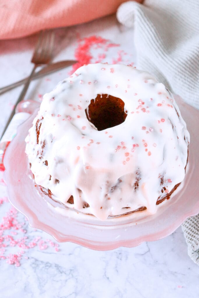 Beautiful bundt cake topped with a glossy pink glaze and delicate sprinkles, displayed on a pink cake stand, offering a whimsical and festive option for Valentine's Cake Ideas.