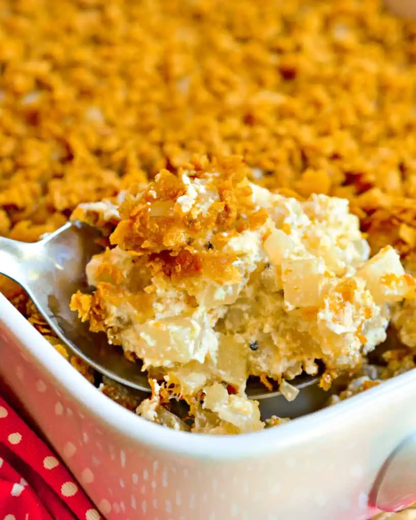 A close-up of creamy hash brown casserole with a crunchy golden topping, being scooped from a baking dish. A comforting and hearty Super Bowl food idea for feeding a crowd.