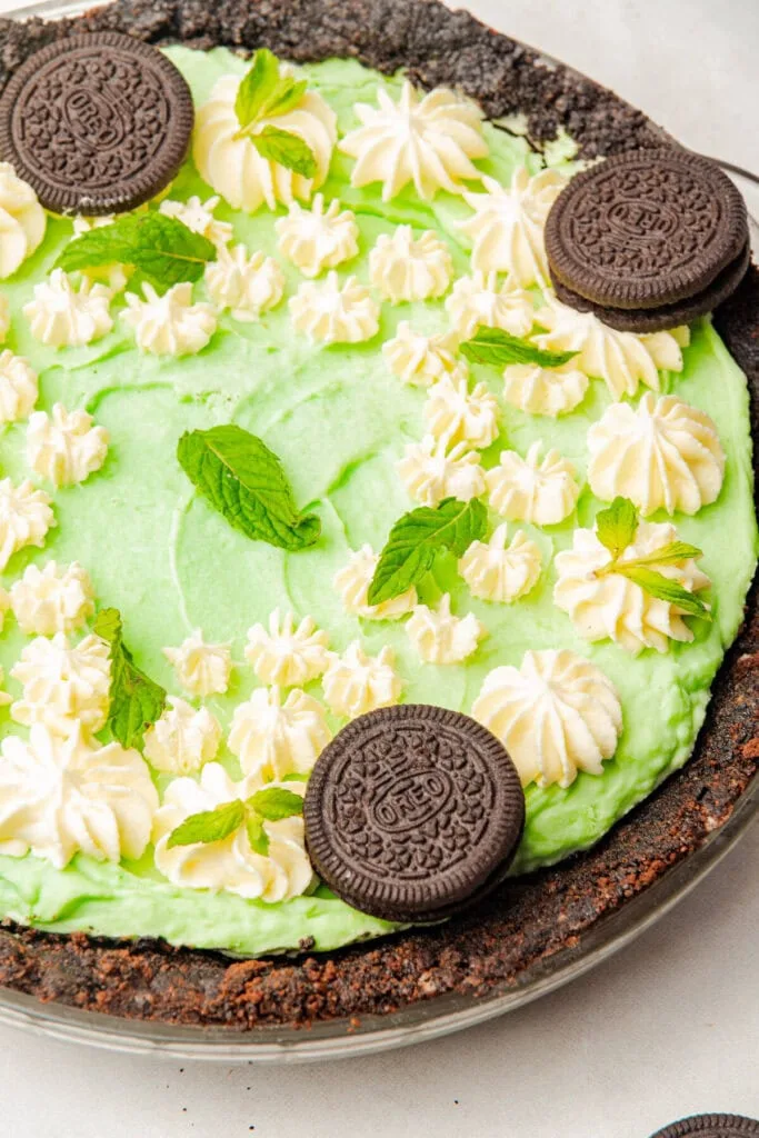 A vibrant no-bake mint pie with a chocolate Oreo crust, whipped cream swirls, fresh mint garnish, and whole Oreo cookies, perfect for Irish desserts or St Patrick's Day celebrations.