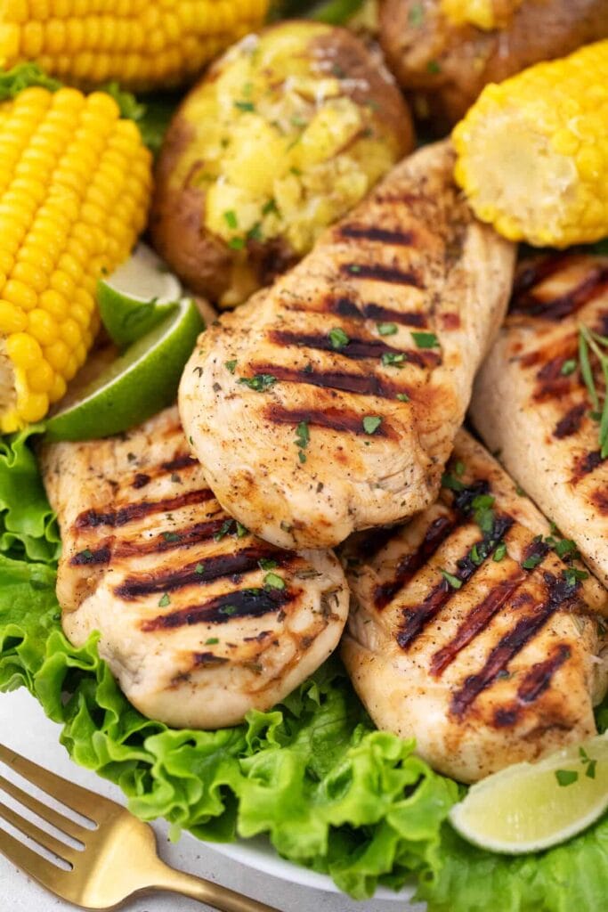 Grilled chicken breasts served on a bed of fresh lettuce with corn on the cob, baked potatoes, and lime wedges, showcasing St. Patrick's Day food ideas and Irish recipes for a hearty and festive meal.