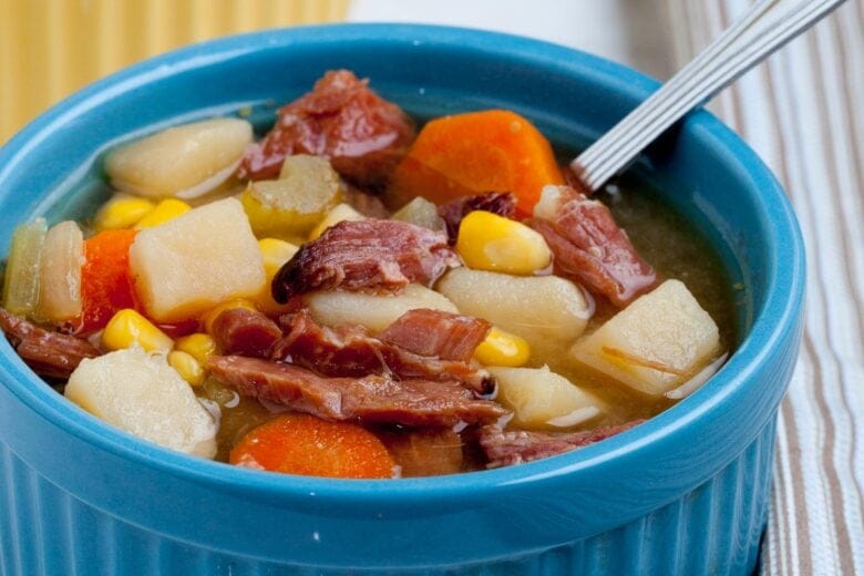 Close-up of a hearty ham and vegetable soup in a blue bowl, filled with tender chunks of ham, potatoes, carrots, and corn—a comforting and flavorful option for leftovers recipes.