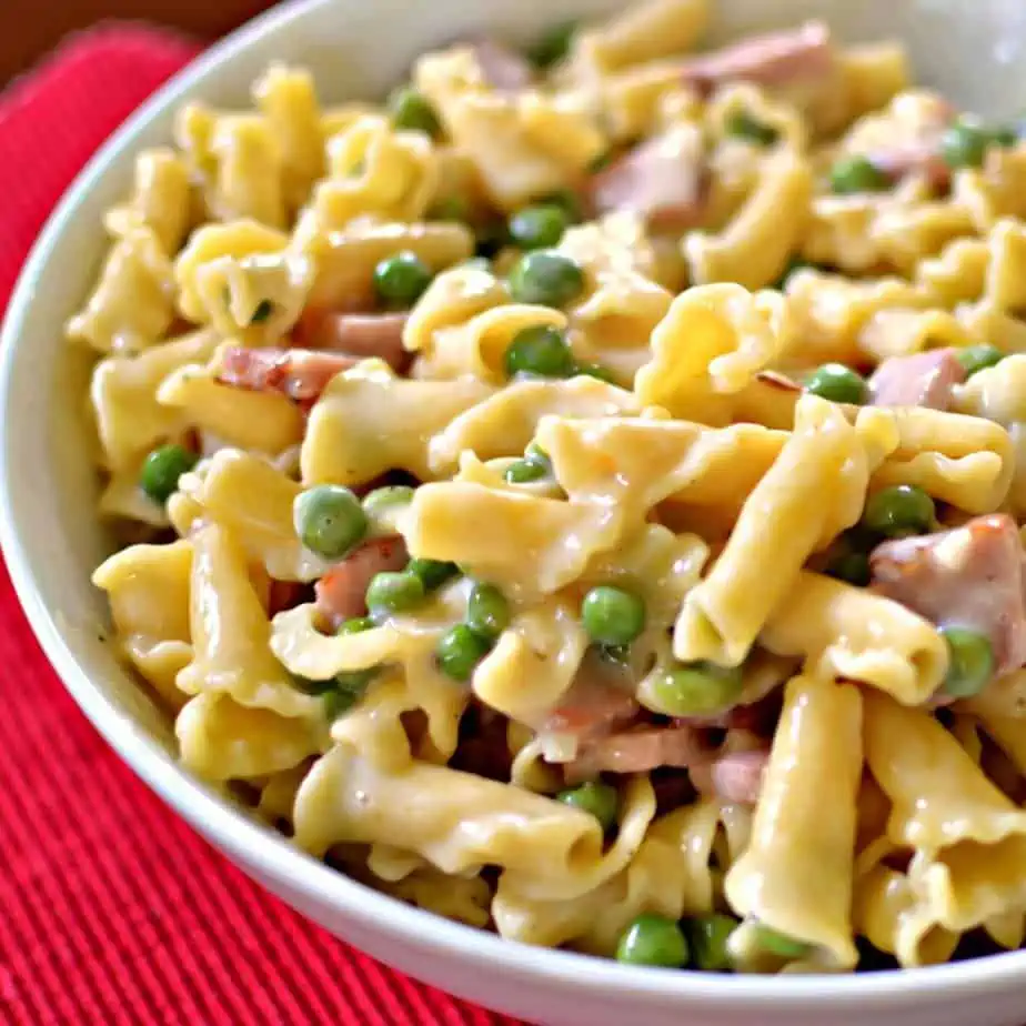 A creamy pasta dish mixed with ham and peas, served in a white bowl. A comforting and easy-to-make Super Bowl food idea for game day meals.