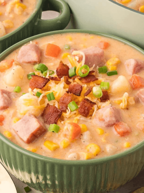 Warm and hearty ham and corn chowder in a green bowl, topped with crispy bacon, shredded cheese, and green onions, ideal for quick meals with ham.