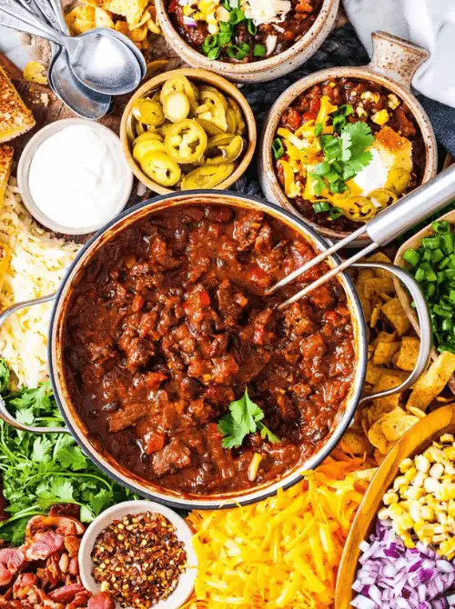 Hearty beef chili surrounded by toppings like cheese, sour cream, jalapeños, and onions—an ultimate Super Bowl food idea for a build-your-own chili bar.