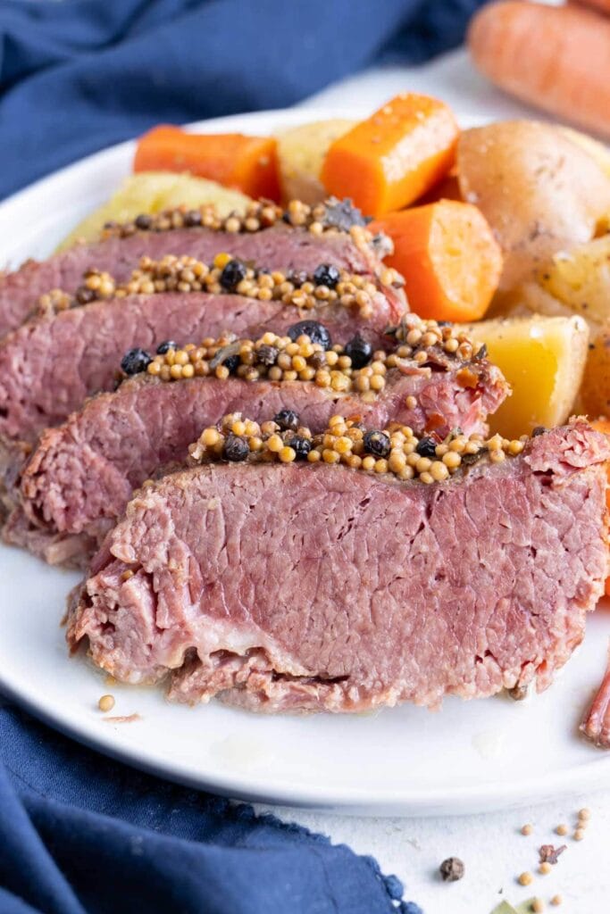 Plate of tender sliced corned beef topped with mustard seeds and spices, served alongside carrots and potatoes, a flavorful dish perfect for St. Patrick's Day food ideas and traditional Irish recipes.