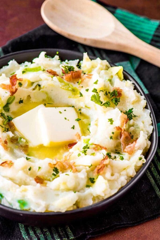 Bowl of creamy Irish colcannon mashed potatoes, mixed with cabbage and topped with crispy bacon, fresh parsley, and a melting pat of butter—ideal for St. Patrick's Day food ideas and traditional Irish recipes.