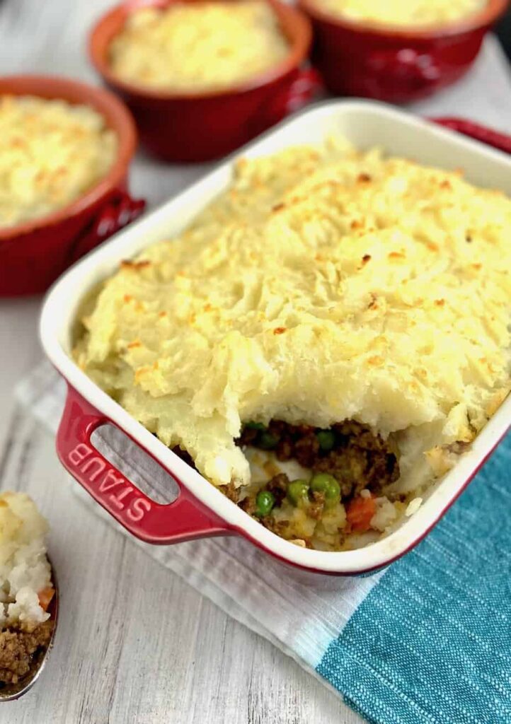 Red baking dish filled with shepherd's pie, featuring a savory meat and vegetable filling topped with creamy mashed potatoes, a classic comfort food perfect for St. Patrick's Day food ideas and Irish-inspired recipes.