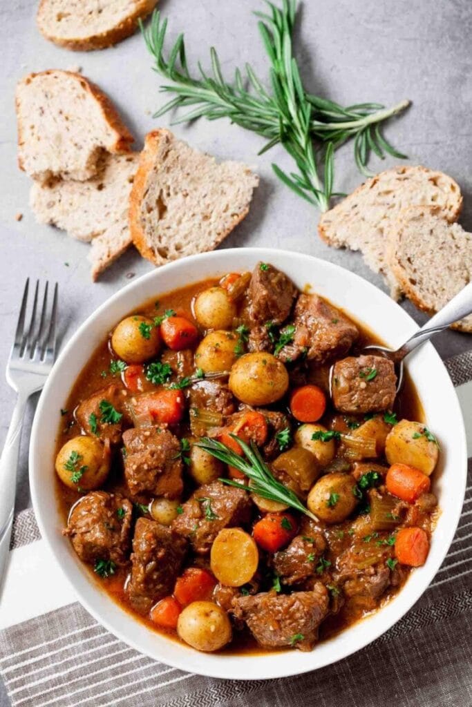 Hearty bowl of Irish beef stew with tender potatoes, carrots, and rich gravy, garnished with fresh rosemary and served with slices of rustic bread—perfect for St. Patrick's Day food ideas and classic Irish recipes.